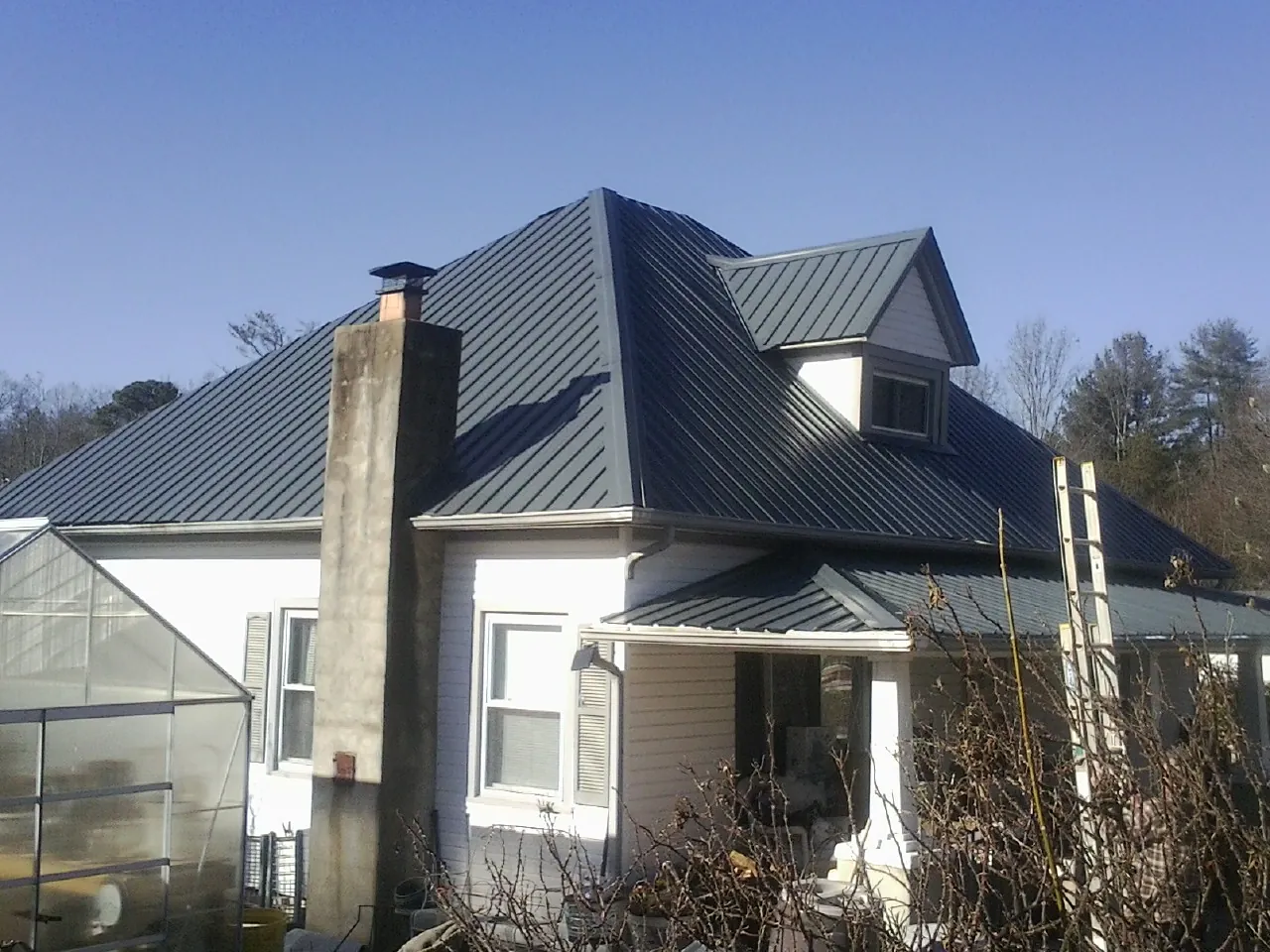 Dark blue standing seam metal roof on a white farmhouse with dormer — Slate & Tile Roof Repair by Roofing Brothers in Mayodan
