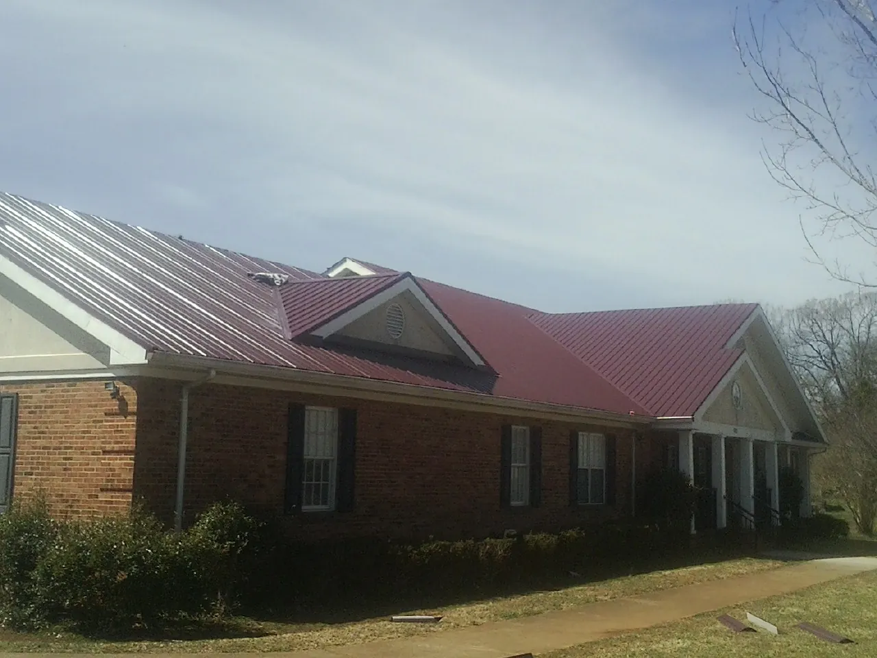 Red metal roof with gabled entries on a long brick building, from a Hail Damage Roof Repair job in Mayodan