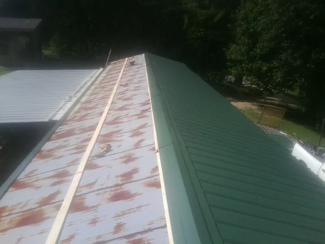 Old rusted panels beside newly installed green metal roofing — Wind Damage Roof Repair by Roofing Brothers in Mayodan