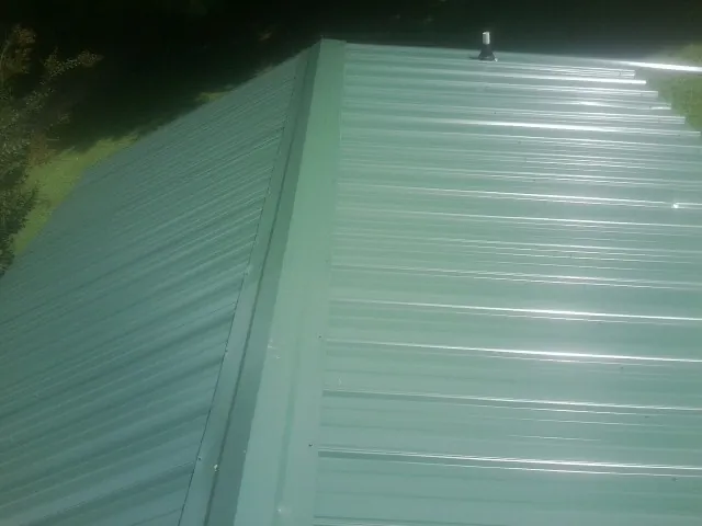 New green metal panels meeting at the ridge of a roof — Flat Roof Repair work by our crew in Mayodan