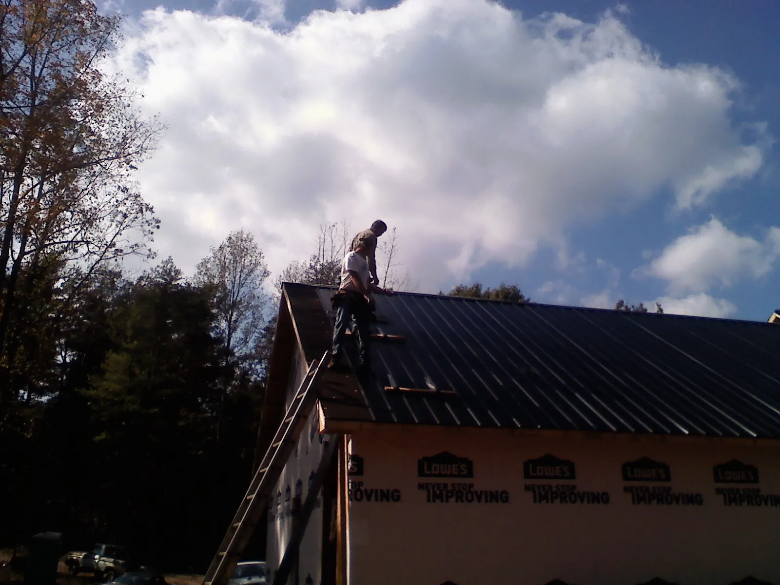 Roofer fastening dark metal panels high against a cloudy sky, from a Roof Inspection job in Mayodan