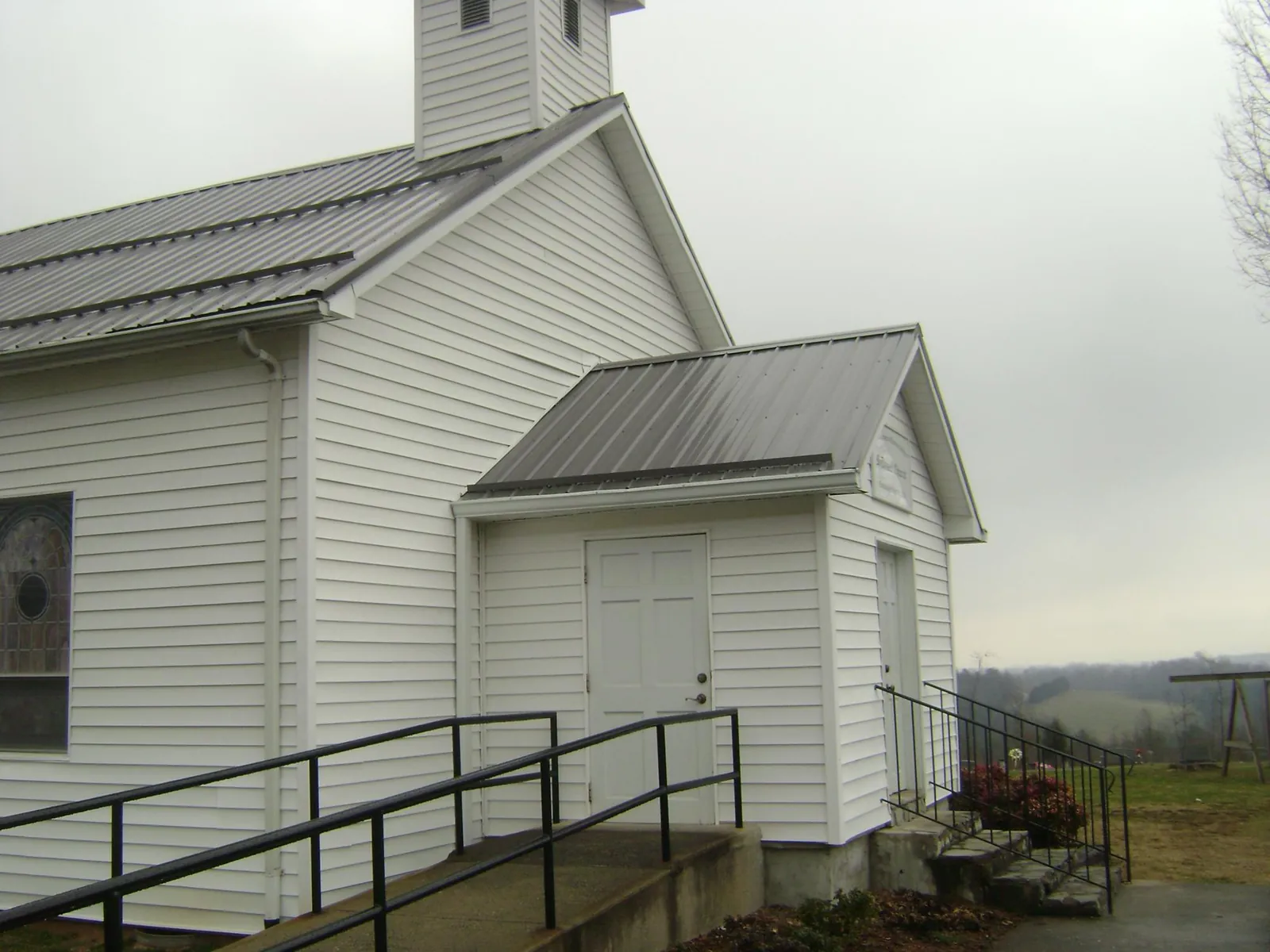 Gray metal roof on a white clapboard church with a steeple in Mayodan
